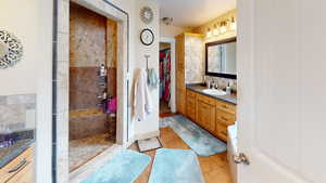 Bathroom with tile patterned floors, tiled shower, backsplash, and vanity