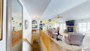 Living room featuring a fireplace, vaulted ceiling, and ceiling fan