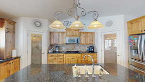 Kitchen with sink, dark stone countertops, stainless steel appliances, and decorative light fixtures