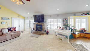 Carpeted living room featuring a fireplace, lofted ceiling, and ceiling fan