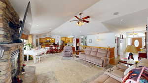 Living room featuring ceiling fan with notable chandelier, vaulted ceiling, and a fireplace