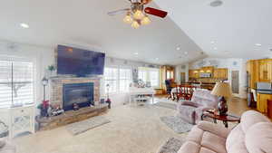 Carpeted living room with ceiling fan, lofted ceiling, and a stone fireplace