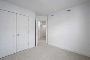 Unfurnished bedroom with visible vents, baseboards, light colored carpet, and a closet