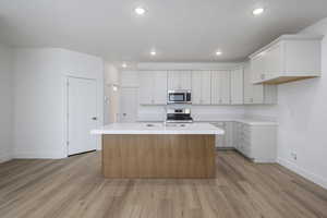 Kitchen with light wood-style floors, appliances with stainless steel finishes, an island with sink, and light countertops