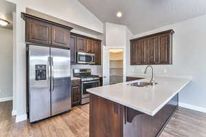 Kitchen featuring lofted ceiling, appliances with stainless steel finishes, sink, light wood-type flooring, and kitchen peninsula