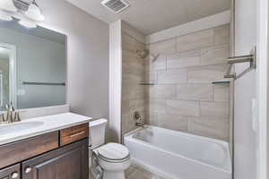 Full bathroom featuring vanity, tiled shower / bath, toilet, and a textured ceiling