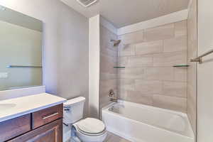 Full bathroom with vanity, tiled shower / bath, toilet, and a textured ceiling