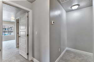 Corridor featuring a textured ceiling and light carpet