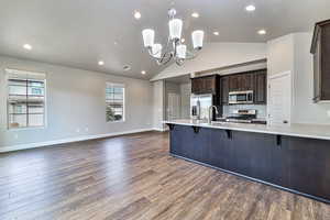 Kitchen featuring hardwood / wood-style floors, appliances with stainless steel finishes, pendant lighting, dark brown cabinets, and a breakfast bar area