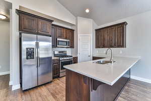 Kitchen with kitchen peninsula, hardwood / wood-style flooring, lofted ceiling, sink, and appliances with stainless steel finishes