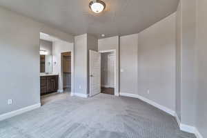 Unfurnished bedroom featuring a closet, ensuite bath, a textured ceiling, light carpet, and a walk in closet