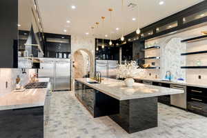 Kitchen with a large island, high quality appliances, light stone countertops, and decorative light fixtures