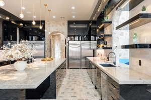 Kitchen with sink, beverage cooler, hanging light fixtures, stainless steel built in fridge, and light stone countertops