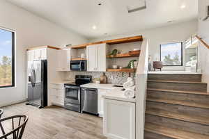 Kitchen featuring white cabinets, light wood-type flooring, stainless steel appliances, and tasteful backsplash