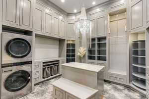 Clothes washing area featuring cabinets, an inviting chandelier, and stacked washer and dryer