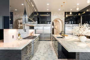 Kitchen featuring sink, high quality appliances, a large island with sink, decorative light fixtures, and light stone countertops