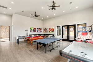 Rec room featuring light hardwood / wood-style floors, french doors, ceiling fan, and a high ceiling