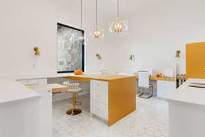 Kitchen with hanging light fixtures, a kitchen island, light tile patterned floors, white cabinets, and built in desk