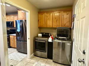 Laundry area with washer and dryer, cabinets, a textured ceiling, and light tile patterned floors