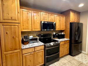 Kitchen featuring decorative backsplash, light tile patterned floors, stainless steel appliances, and light stone counters