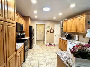 Kitchen with a textured ceiling, light tile patterned flooring, light stone countertops, and black appliances