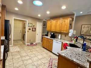 Kitchen with dishwasher, light stone countertops, stainless steel refrigerator, light tile patterned floors, and sink