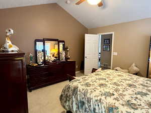 Carpeted bedroom featuring vaulted ceiling, ceiling fan, and a textured ceiling