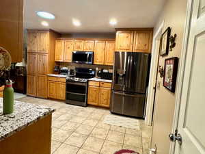 Kitchen with appliances with stainless steel finishes, light stone counters, and light tile patterned floors