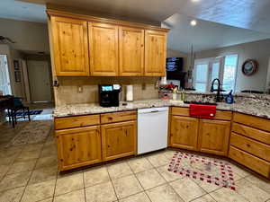 Kitchen with kitchen peninsula, lofted ceiling, sink, white dishwasher, and light tile patterned flooring