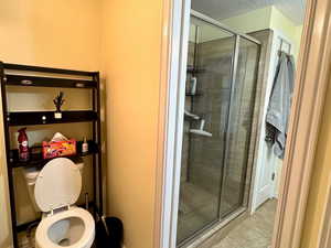 Bathroom featuring toilet, an enclosed shower, and a textured ceiling