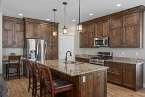 Kitchen featuring a center island with sink, appliances with stainless steel finishes, sink, light stone counters, and pendant lighting