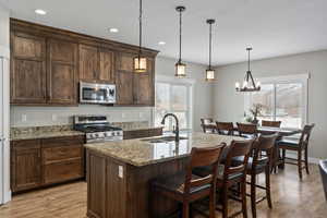 Kitchen featuring appliances with stainless steel finishes, an island with sink, light stone counters, pendant lighting, and sink