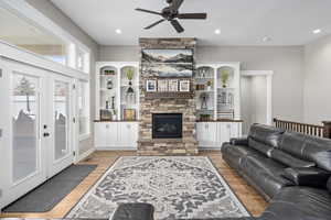 Living room with ceiling fan, light hardwood / wood-style flooring, a stone fireplace, and french doors