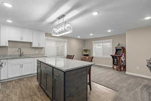 Kitchen featuring white cabinetry, sink, light stone counters, and pendant lighting