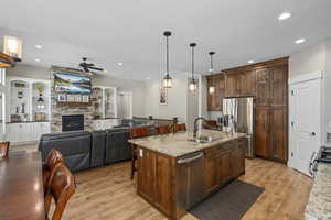 Kitchen with an island with sink, stainless steel appliances, decorative light fixtures, sink, and light stone counters