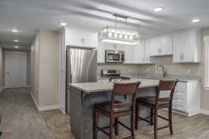 Kitchen featuring white cabinetry, stainless steel appliances, sink, a kitchen breakfast bar, and pendant lighting