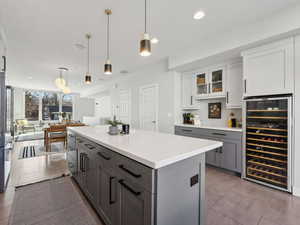 Kitchen with pendant lighting, white cabinetry, gray cabinetry, stainless steel microwave, and beverage cooler