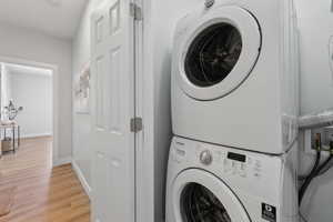 Laundry room with stacked washer / dryer and light hardwood / wood-style flooring