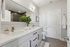 Ensuite bathroom featuring dual vanity, a shower with shower door, and toilet