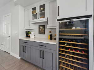 Bar featuring white cabinets, gray cabinetry, wine cooler, and light hardwood / wood-style flooring