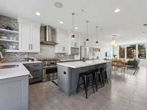 Kitchen featuring sink, white cabinets, premium appliances, a center island, and wall chimney range hood