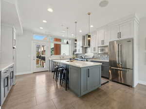 Kitchen with appliances with stainless steel finishes, gray cabinetry, hanging light fixtures, a center island, and wall chimney range hood