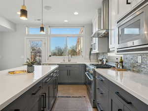 Kitchen featuring sink, decorative light fixtures, appliances with stainless steel finishes, wall chimney range hood, and backsplash