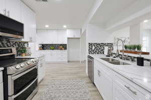 Kitchen featuring appliances with stainless steel finishes, sink, white cabinetry, light stone countertops, and decorative backsplash