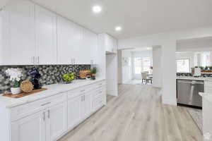 Kitchen with white cabinetry, light hardwood / wood-style flooring, backsplash, light stone counters, and dishwasher