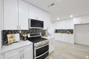 Kitchen with light stone counters, white cabinetry, light hardwood / wood-style floors, stainless steel appliances, and tasteful backsplash