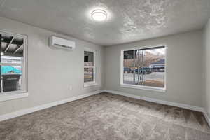 Spare room featuring a wall unit AC, carpet flooring, a textured ceiling, and a healthy amount of sunlight