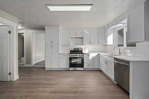 Kitchen with sink, white cabinets, stainless steel appliances, and light hardwood / wood-style floors