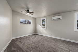 Carpeted spare room with ceiling fan, an AC wall unit, and a textured ceiling