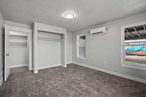 Unfurnished bedroom featuring a textured ceiling, dark colored carpet, a closet, and a wall unit AC